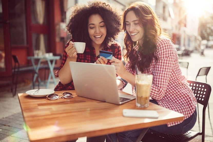 Two women looking at a credit card and computer while sitting outside at a restaurant